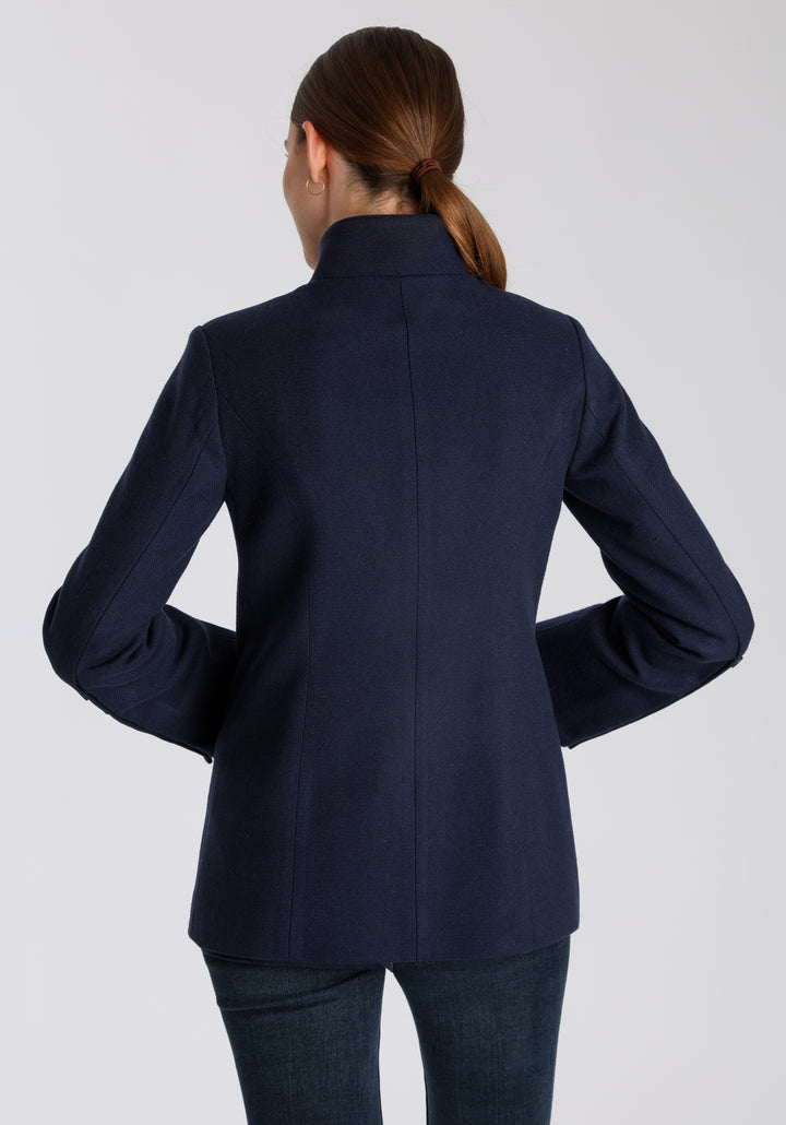 Model wearing the Patmos jacket in textured navy merino wool with suede trim, a slim-fit style featuring a mandarin collar, front pockets, and generous sleeves with button detailing.
