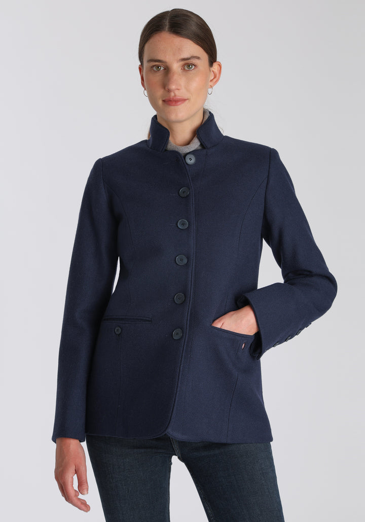 Model wearing the Patmos jacket in textured navy merino wool with suede trim, a slim-fit style featuring a mandarin collar, front pockets, and generous sleeves with button detailing.