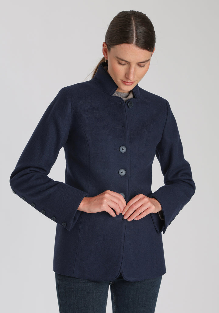 Model wearing the Patmos jacket in textured navy merino wool with suede trim, a slim-fit style featuring a mandarin collar, front pockets, and generous sleeves with button detailing.