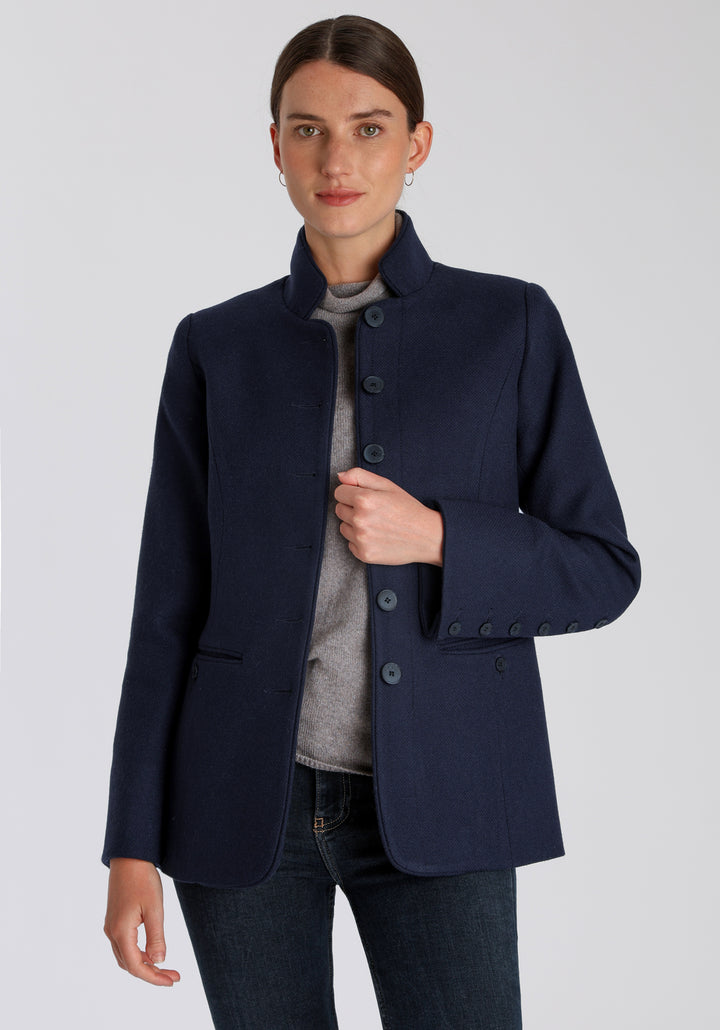 Model wearing the Patmos jacket in textured navy merino wool with suede trim, a slim-fit style featuring a mandarin collar, front pockets, and generous sleeves with button detailing.