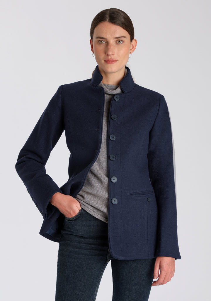 Model wearing the Patmos jacket in textured navy merino wool with suede trim, a slim-fit style featuring a mandarin collar, front pockets, and generous sleeves with button detailing.