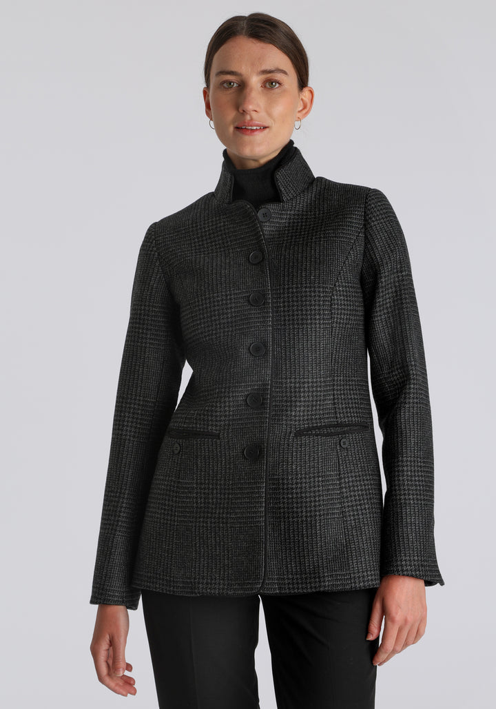 Model wearing the Patmos jacket in black and grey Prince of Wales check with suede trim, a slim-fit style featuring a mandarin collar, front pockets, and generous sleeves with slate button detailing.