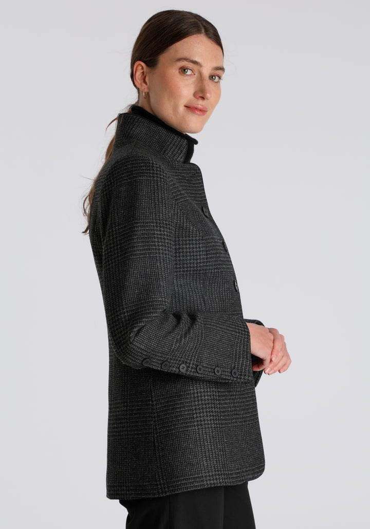 Model wearing the Patmos jacket in black and grey Prince of Wales check with suede trim, a slim-fit style featuring a mandarin collar, front pockets, and generous sleeves with slate button detailing.