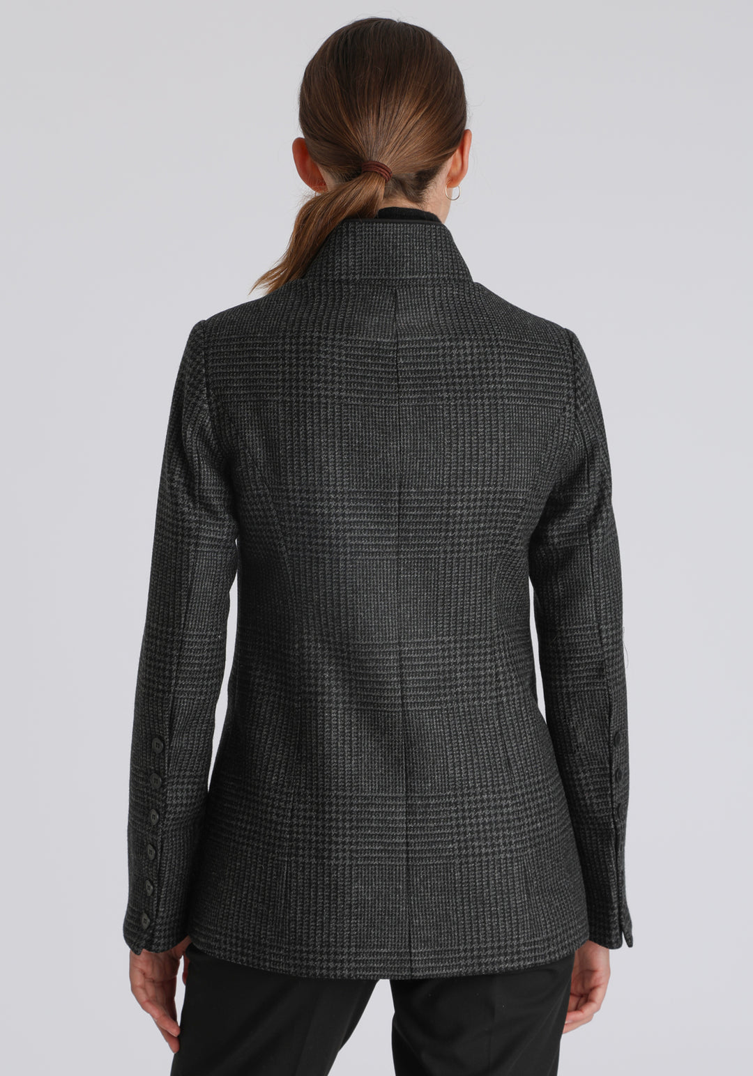 Model wearing the Patmos jacket in black and grey Prince of Wales check with suede trim, a slim-fit style featuring a mandarin collar, front pockets, and generous sleeves with slate button detailing.
