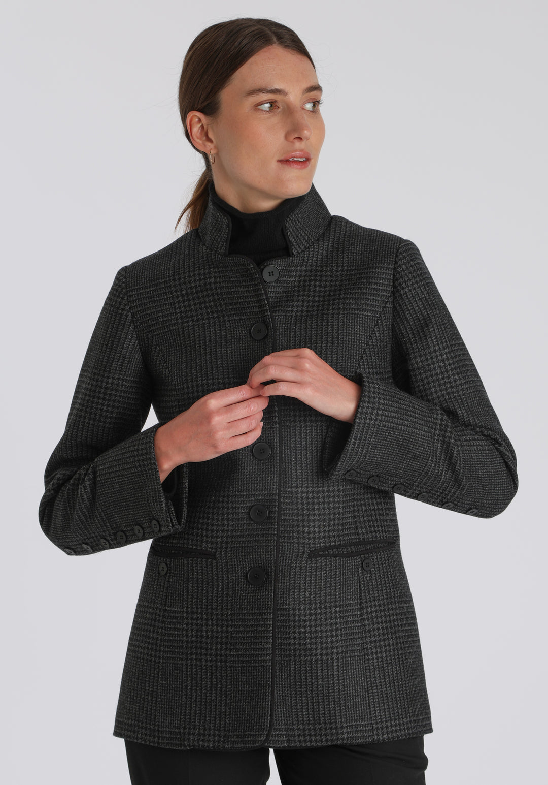 Model wearing the Patmos jacket in black and grey Prince of Wales check with suede trim, a slim-fit style featuring a mandarin collar, front pockets, and generous sleeves with slate button detailing.