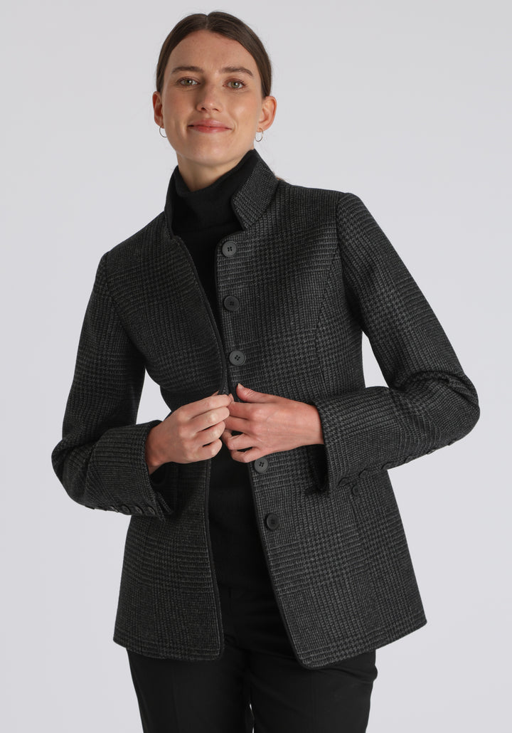 Model wearing the Patmos jacket in black and grey Prince of Wales check with suede trim, a slim-fit style featuring a mandarin collar, front pockets, and generous sleeves with slate button detailing.