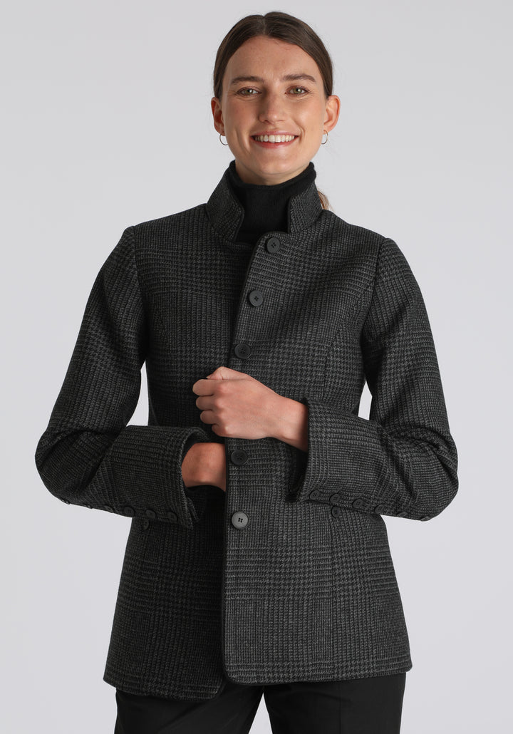 Model wearing the Patmos jacket in black and grey Prince of Wales check with suede trim, a slim-fit style featuring a mandarin collar, front pockets, and generous sleeves with slate button detailing.