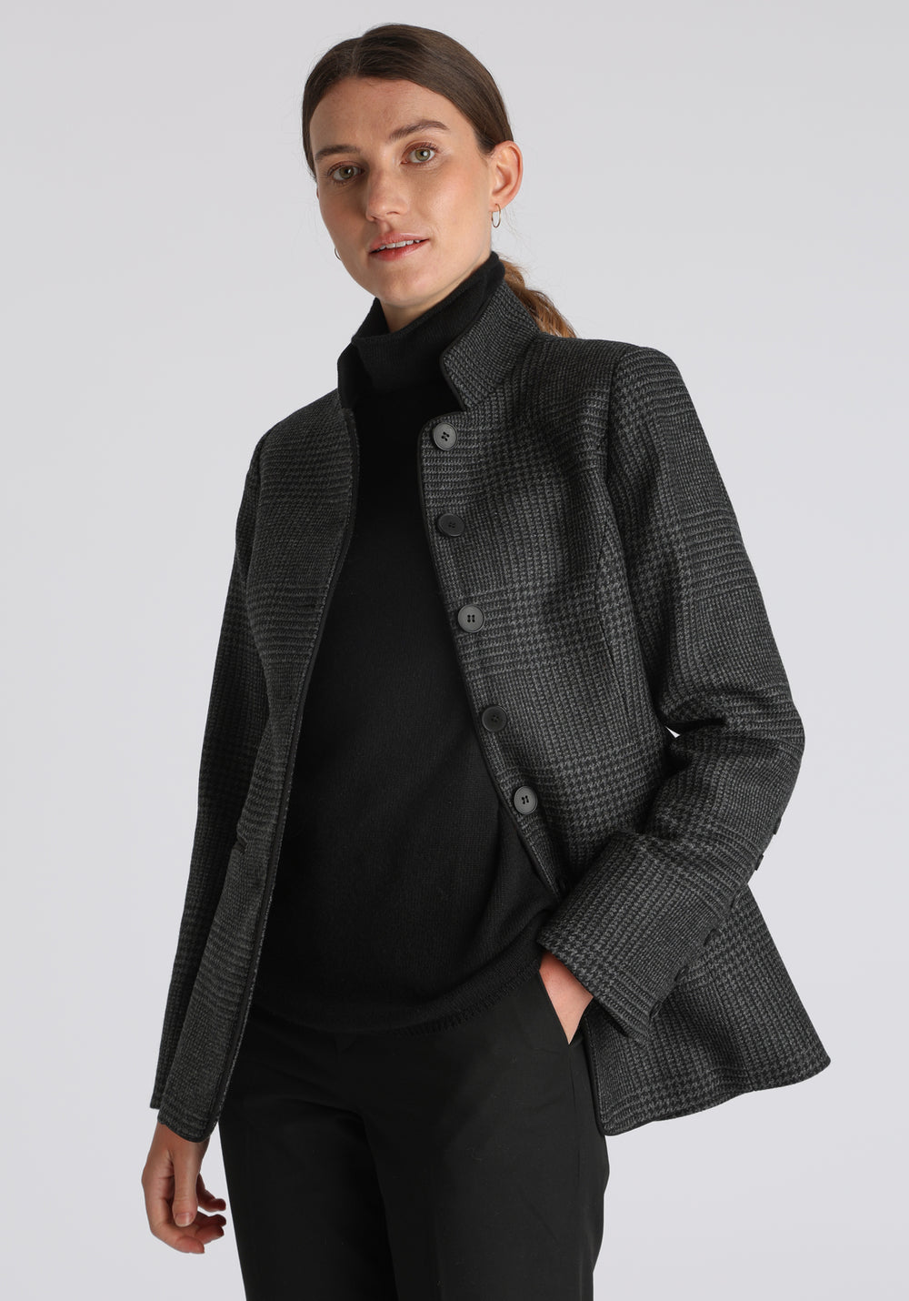 Model wearing the Patmos jacket in black and grey Prince of Wales check with suede trim, a slim-fit style featuring a mandarin collar, front pockets, and generous sleeves with slate button detailing.