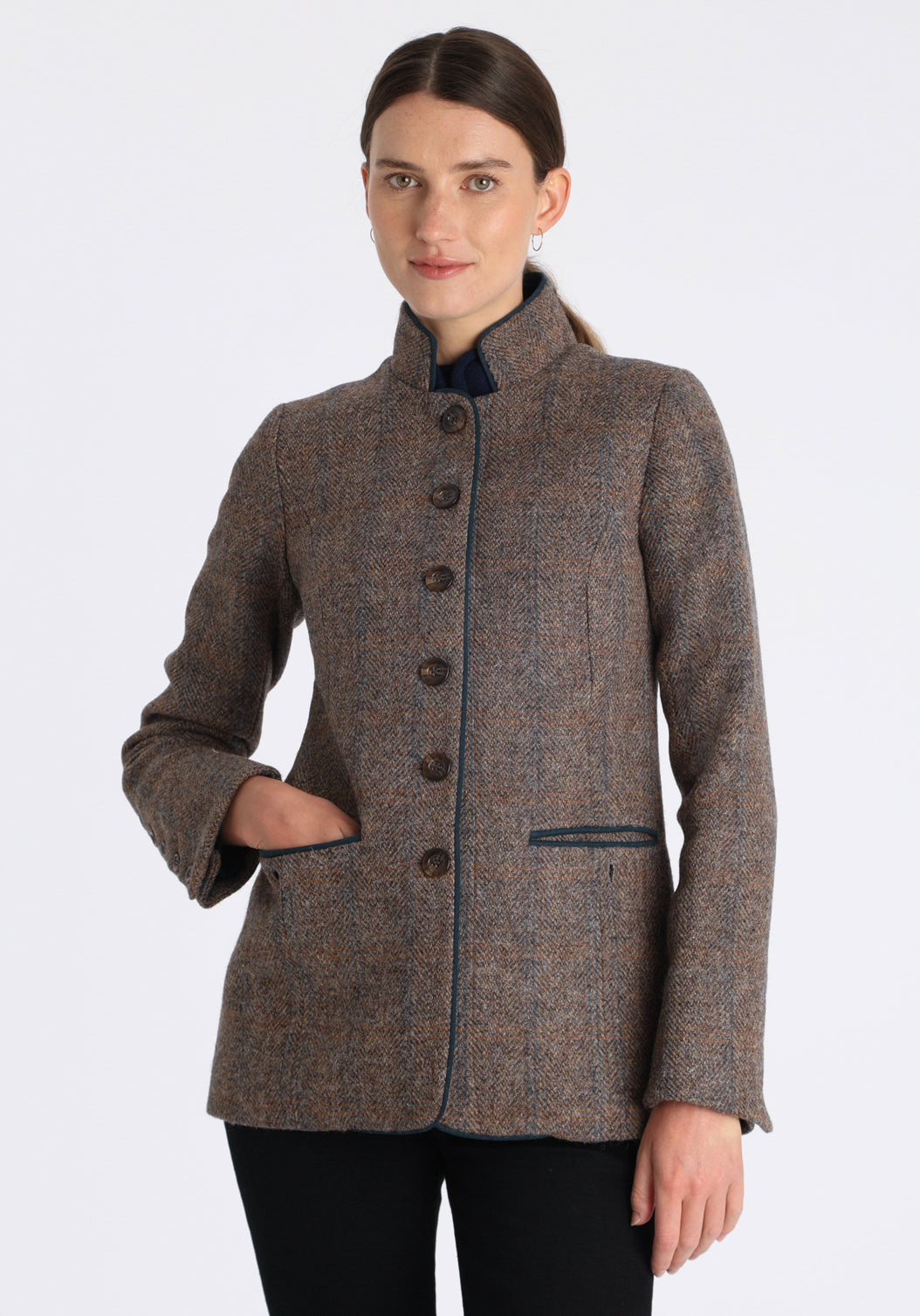 Model wearing the Patmos jacket in a Harris Tweed Clay check, with peach, grey, and brown tones, it features petrol blue suede detailing, a slim fit style featuring a mandarin collar, front pockets, and generous sleeves with button detailing.