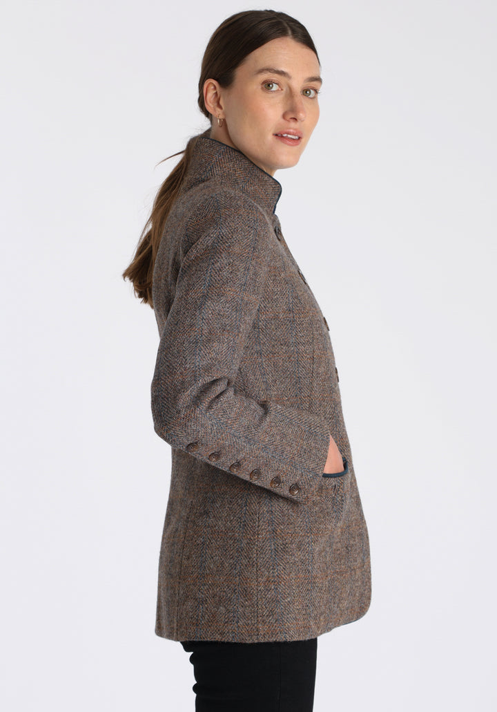 Model wearing the Patmos jacket in a Harris Tweed Clay check, with peach, grey, and brown tones, it features petrol blue suede detailing, a slim fit style featuring a mandarin collar, front pockets, and generous sleeves with button detailing.