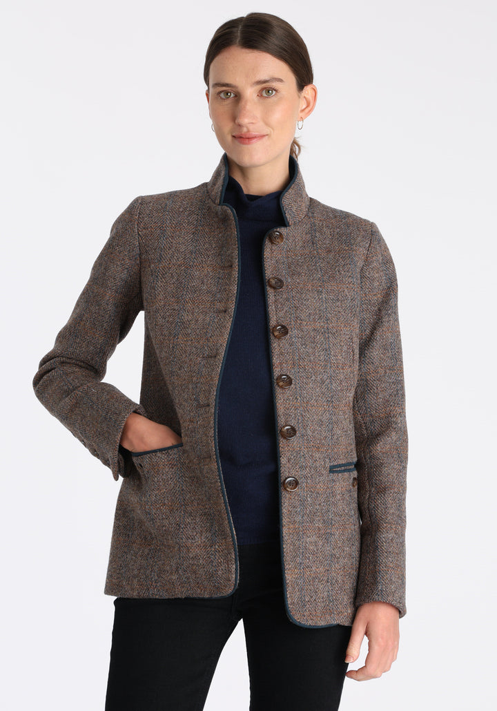 Model wearing the Patmos jacket in a Harris Tweed Clay check, with peach, grey, and brown tones, it features petrol blue suede detailing, a slim fit style featuring a mandarin collar, front pockets, and generous sleeves with button detailing.