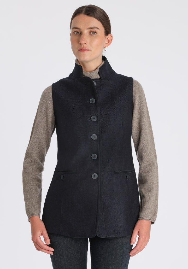 Model wearing the Patmos waistcoat in navy herringbone lambswool with suede trim, a longline, neatly tailored style with a mandarin collar.