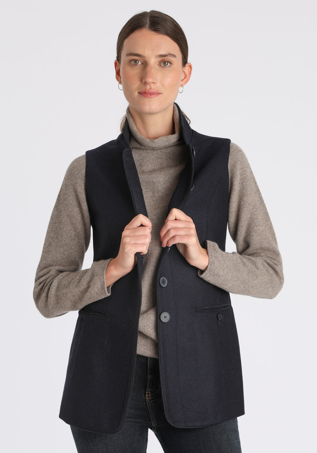 Model wearing the Patmos waistcoat in navy herringbone lambswool with suede trim, a longline, neatly tailored style with a mandarin collar.