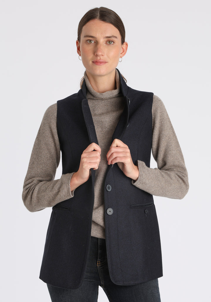 Model wearing the Patmos waistcoat in navy herringbone lambswool with suede trim, a longline, neatly tailored style with a mandarin collar.