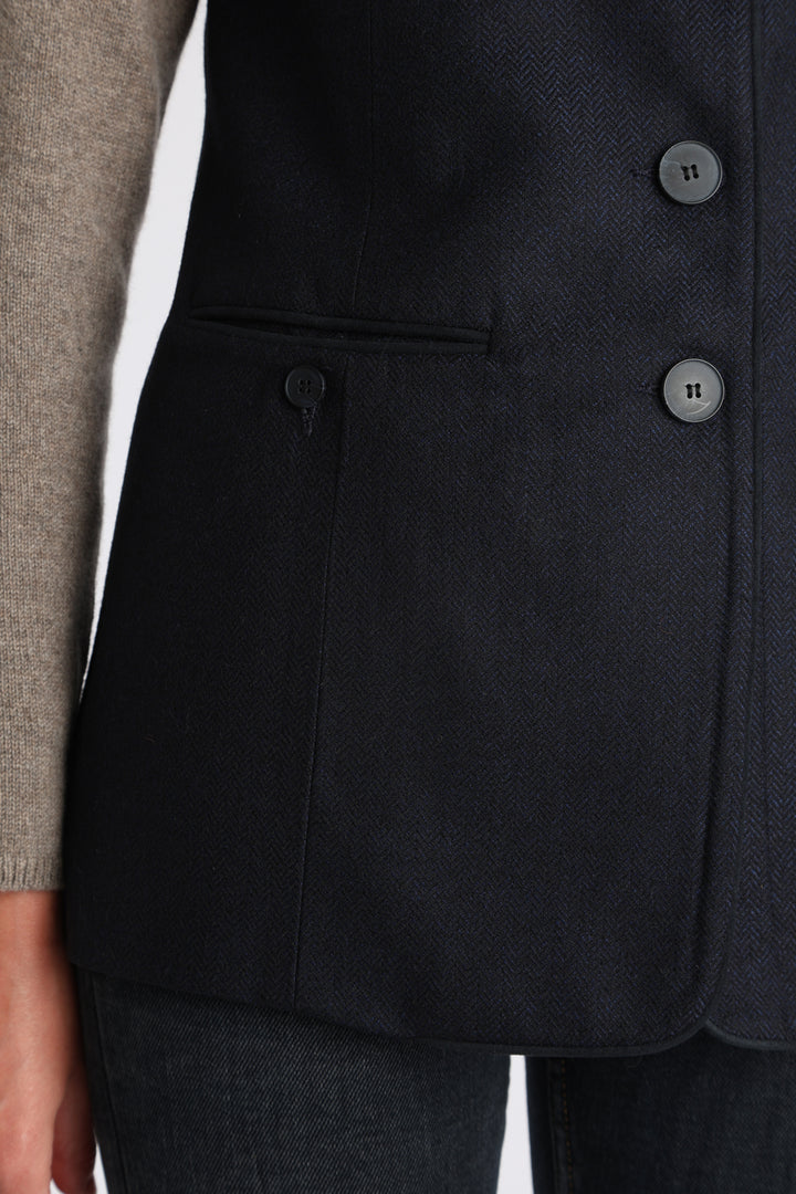 Model wearing the Patmos waistcoat in navy herringbone lambswool with suede trim, a longline, neatly tailored style with a mandarin collar.