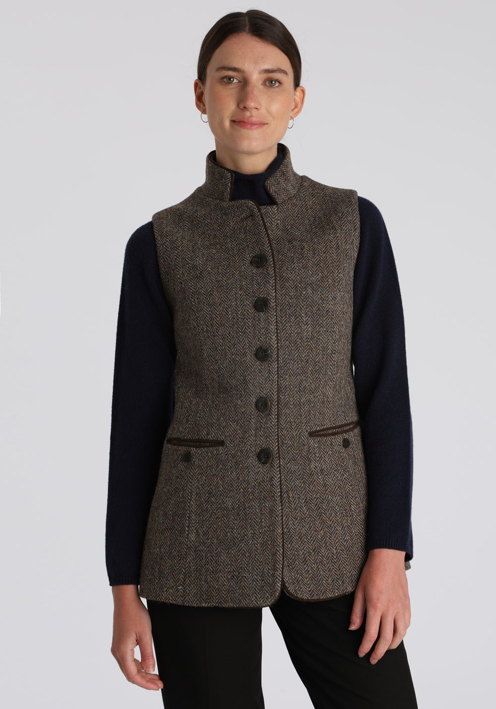 Model wearing the Patmos waistcoat in heather herringbone Harris Tweed with suede trim, a longline, neatly tailored style with a mandarin collar.