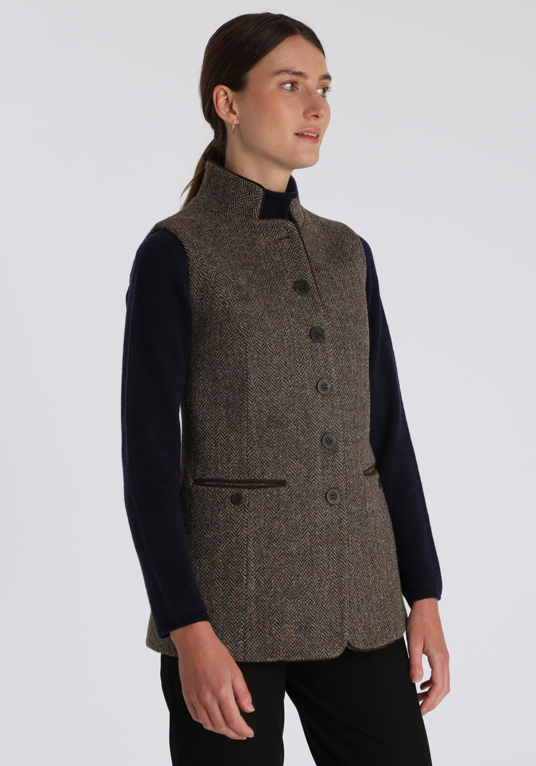 Model wearing the Patmos waistcoat in heather herringbone Harris Tweed with suede trim, a longline, neatly tailored style with a mandarin collar.