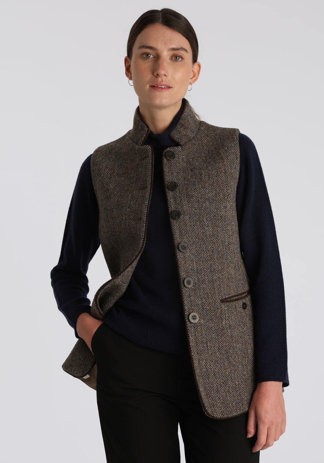 Model wearing the Patmos waistcoat in heather herringbone Harris Tweed with suede trim, a longline, neatly tailored style with a mandarin collar.