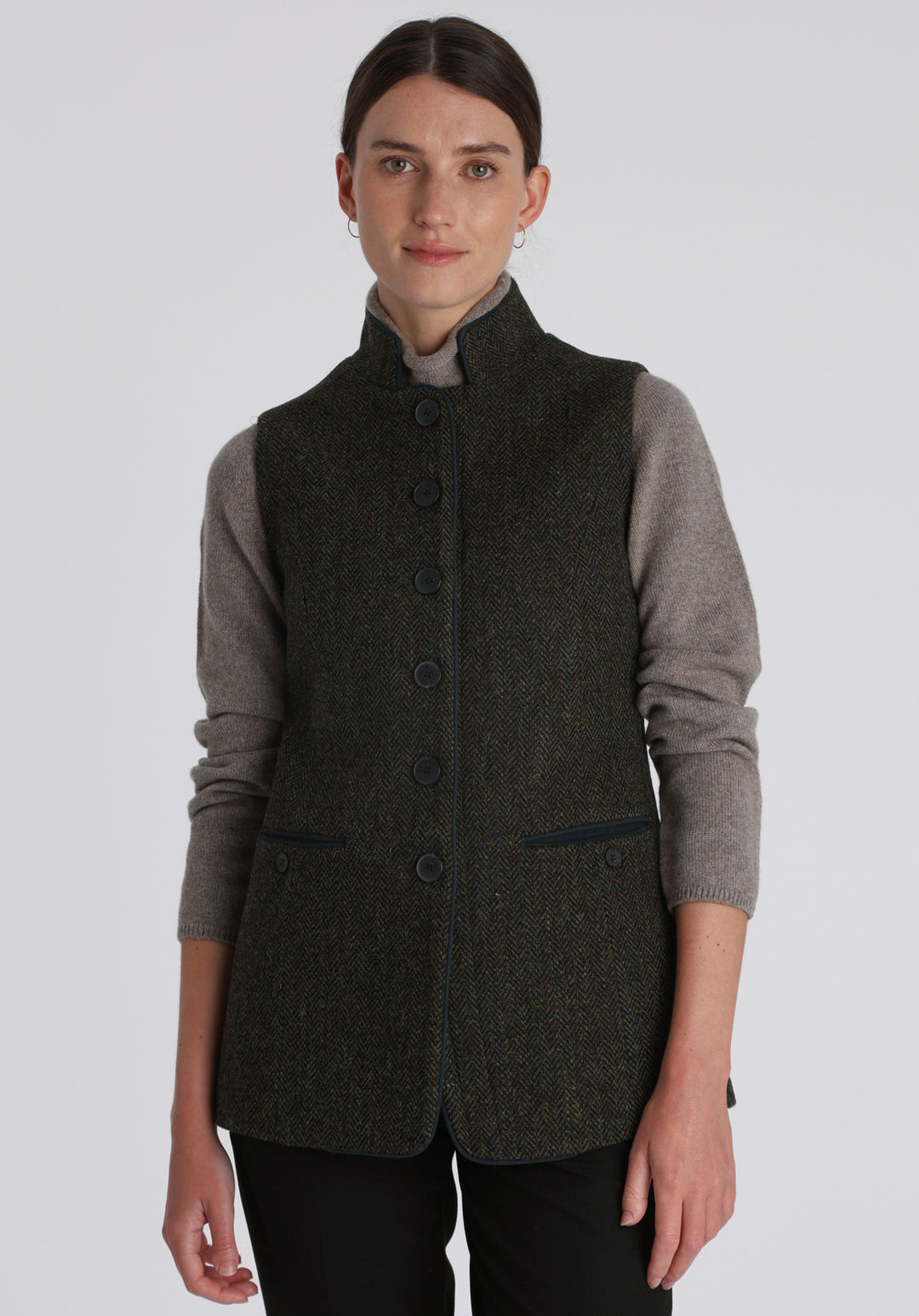 Model wearing the Patmos waistcoat in green spruce herringbone Harris Tweed with suede trim, a longline, neatly tailored style with a mandarin collar.