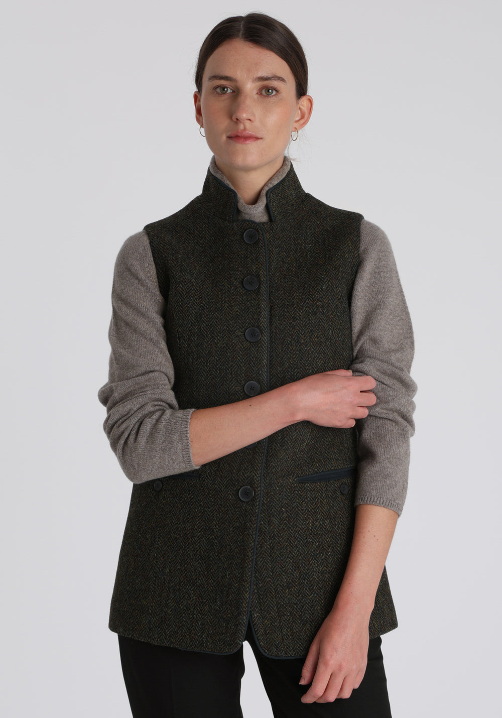 Model wearing the Patmos waistcoat in green spruce herringbone Harris Tweed with suede trim, a longline, neatly tailored style with a mandarin collar.
