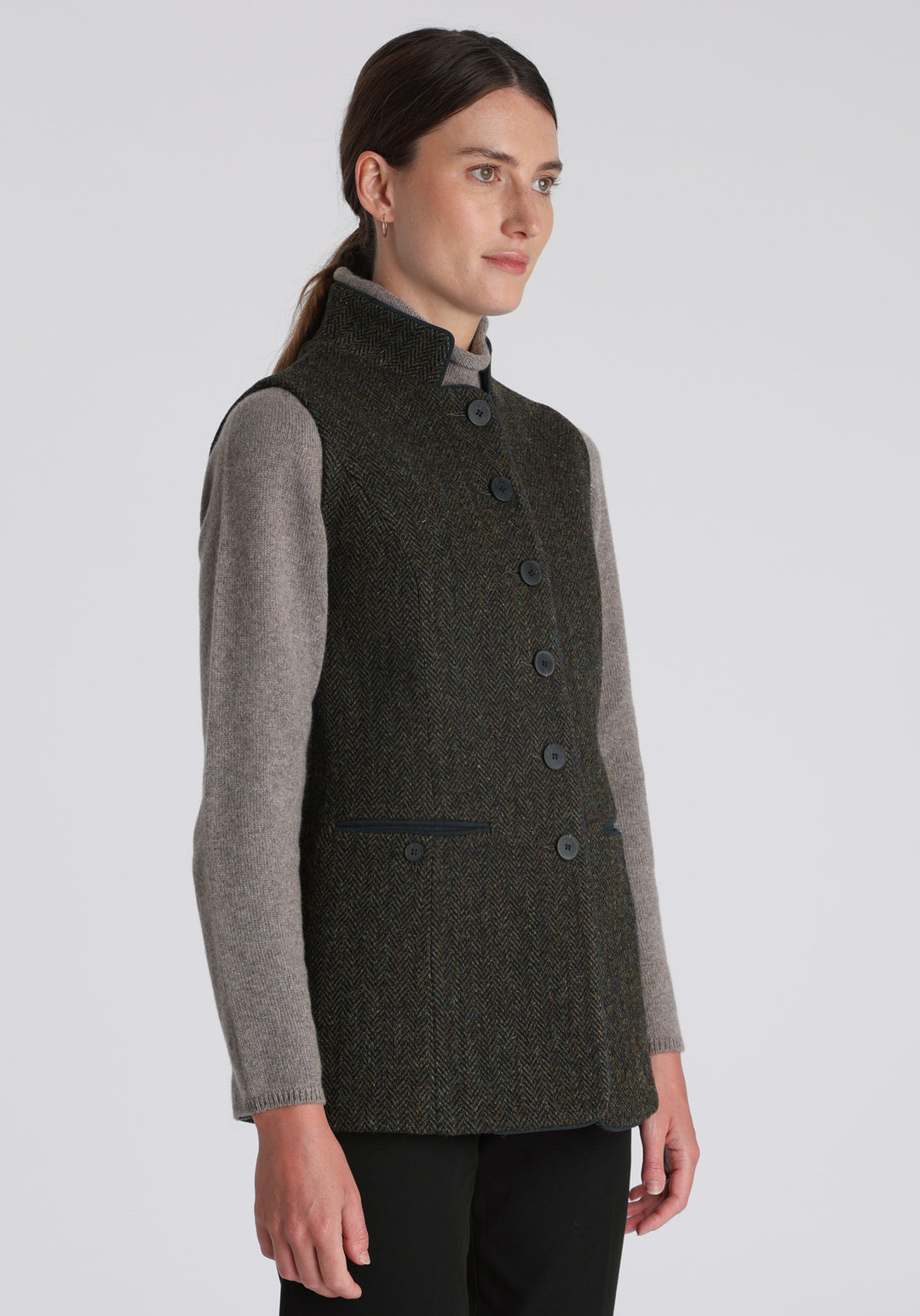 Model wearing the Patmos waistcoat in green spruce herringbone Harris Tweed with suede trim, a longline, neatly tailored style with a mandarin collar.
