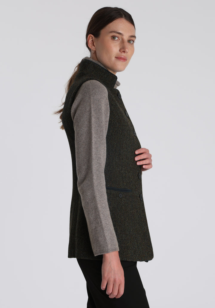 Model wearing the Patmos waistcoat in green spruce herringbone Harris Tweed with suede trim, a longline, neatly tailored style with a mandarin collar.