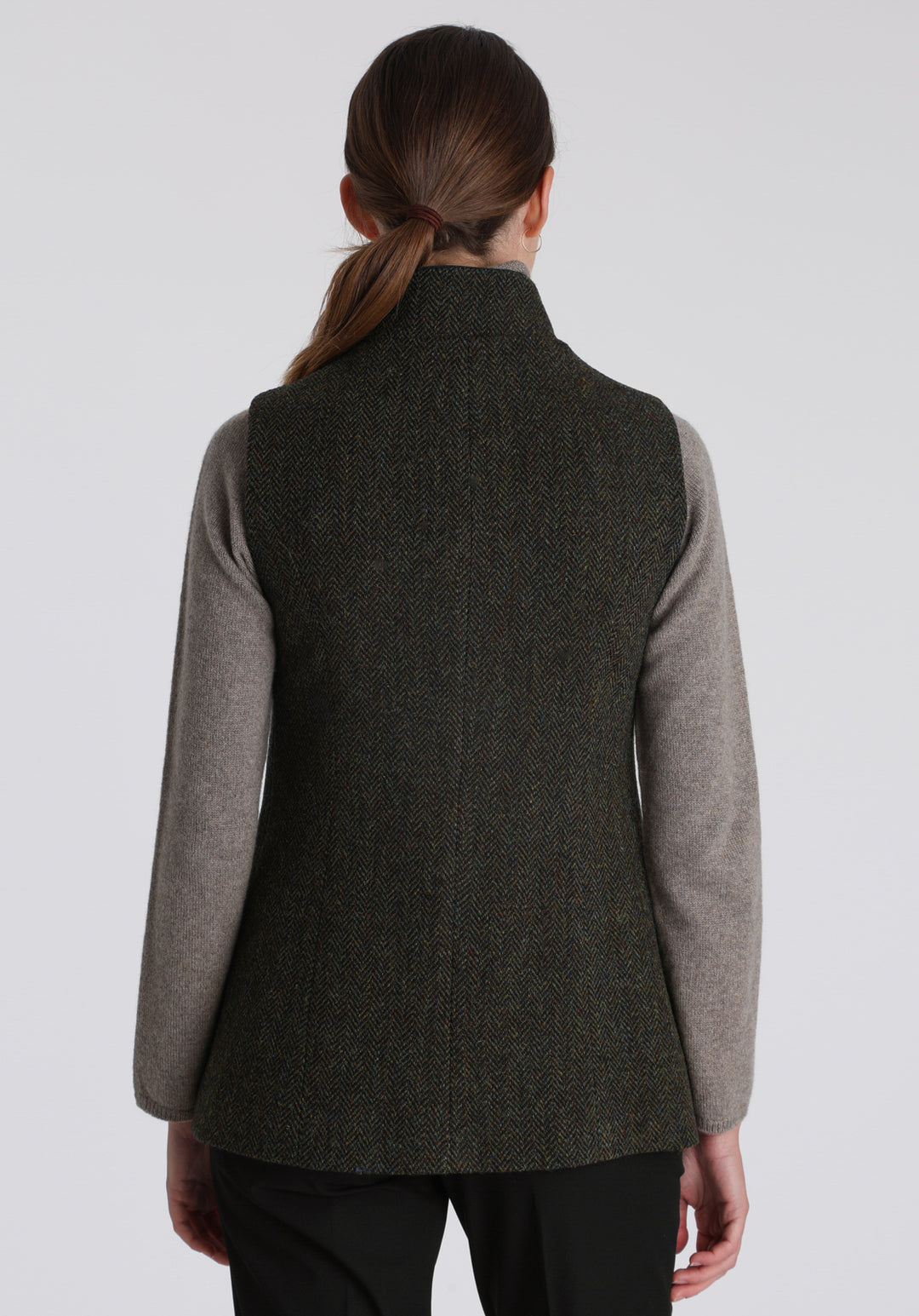 Model wearing the Patmos waistcoat in green spruce herringbone Harris Tweed with suede trim, a longline, neatly tailored style with a mandarin collar.