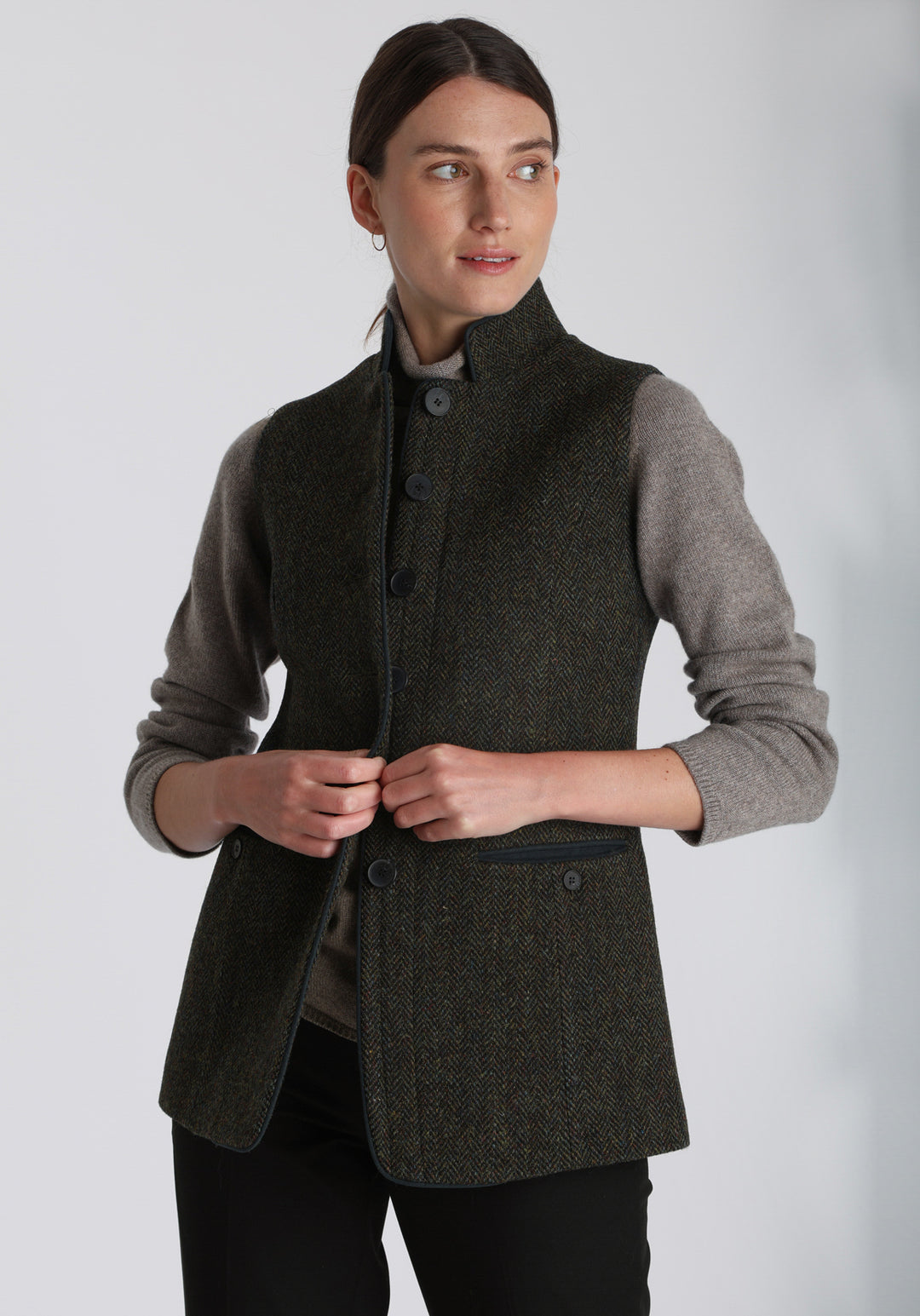 Model wearing the Patmos waistcoat in green spruce herringbone Harris Tweed with suede trim, a longline, neatly tailored style with a mandarin collar.