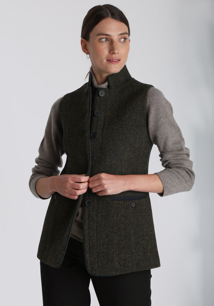 Model wearing the Patmos waistcoat in green spruce herringbone Harris Tweed with suede trim, a longline, neatly tailored style with a mandarin collar.