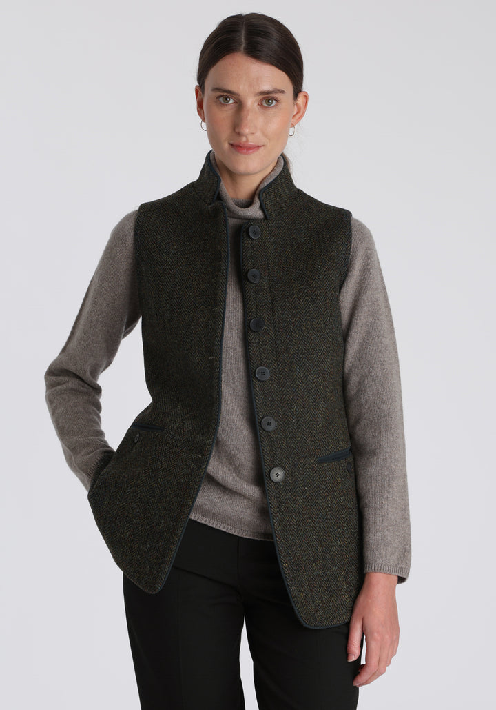 Model wearing the Patmos waistcoat in green spruce herringbone Harris Tweed with suede trim, a longline, neatly tailored style with a mandarin collar.
