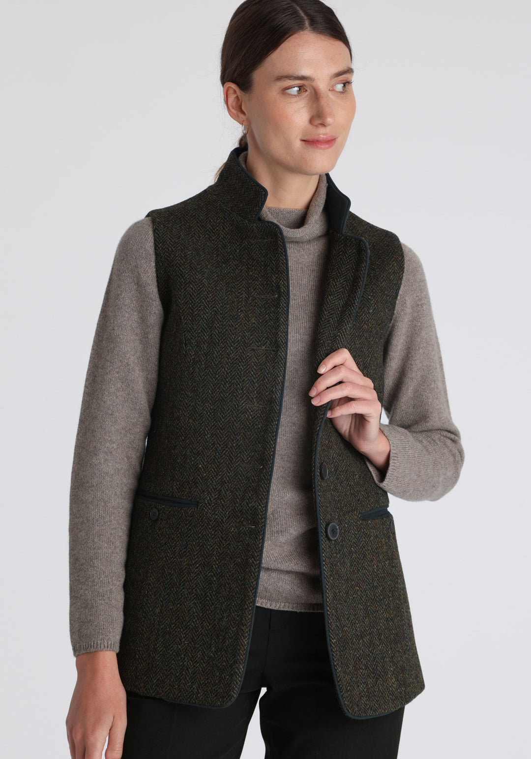 Model wearing the Patmos waistcoat in green spruce herringbone Harris Tweed with suede trim, a longline, neatly tailored style with a mandarin collar.