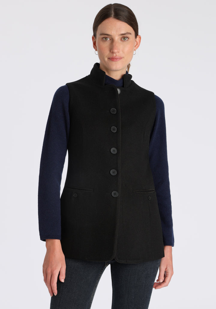 Model wearing the Patmos waistcoat in black textured merino wool with suede trim, a longline, neatly tailored style with a mandarin collar.