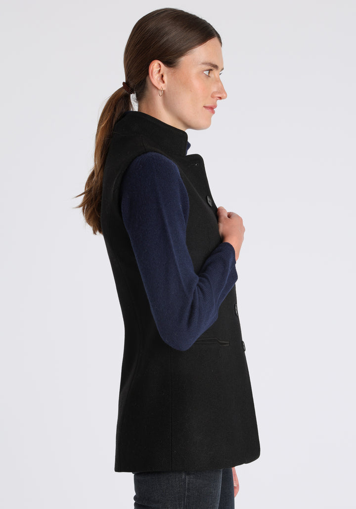 Model wearing the Patmos waistcoat in black textured merino wool with suede trim, a longline, neatly tailored style with a mandarin collar.