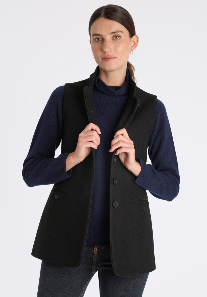 Model wearing the Patmos waistcoat in black textured merino wool with suede trim, a longline, neatly tailored style with a mandarin collar.