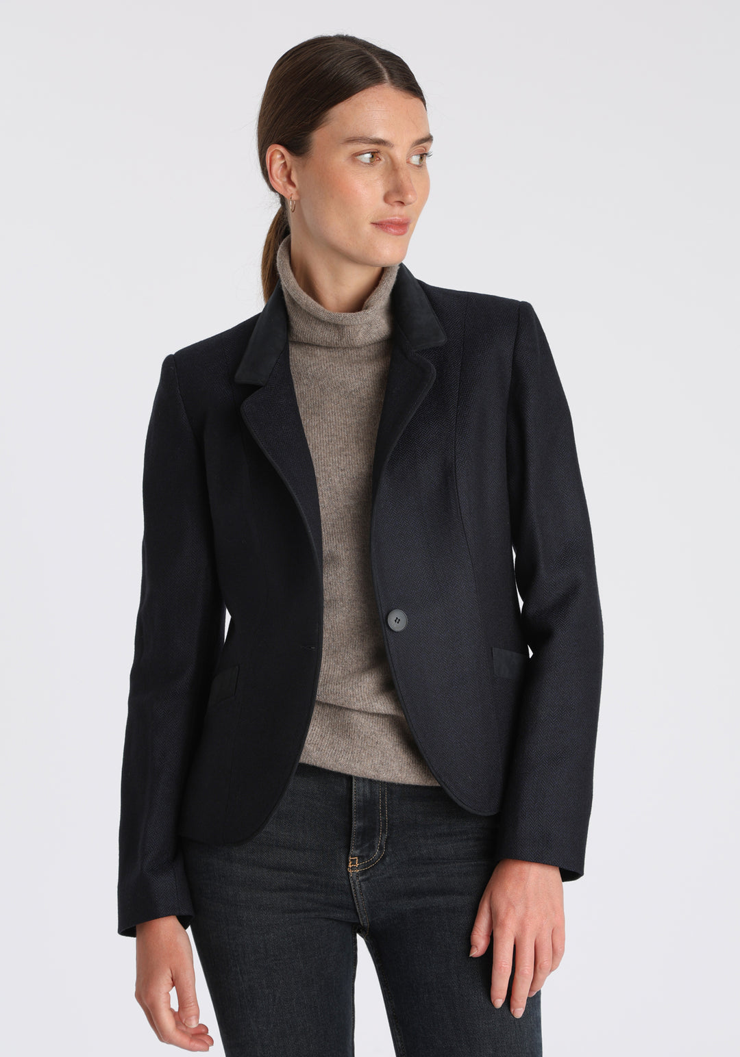 Model wearing the Tallulah jacket in navy herringbone lambswool with suede trim, a tailored style with a single button fastening and a collar that can be worn turned up or down.