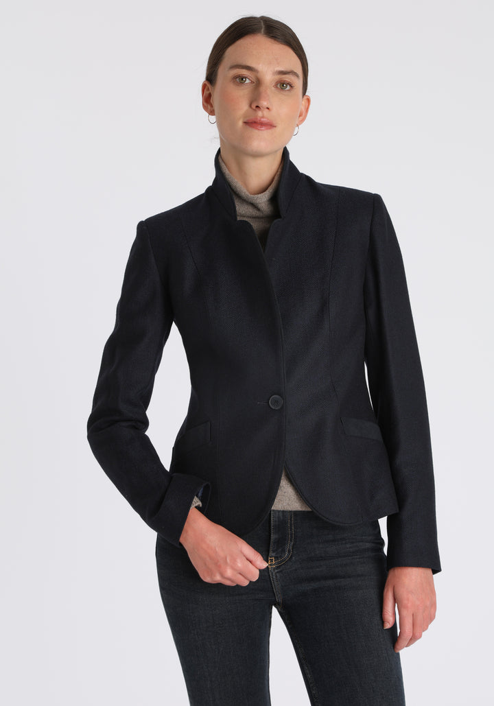 Model wearing the Tallulah jacket in navy herringbone lambswool with suede trim, a tailored style with a single button fastening and a collar that can be worn turned up or down.