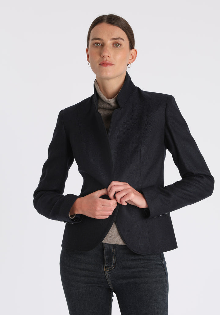 Model wearing the Tallulah jacket in navy herringbone lambswool with suede trim, a tailored style with a single button fastening and a collar that can be worn turned up or down.