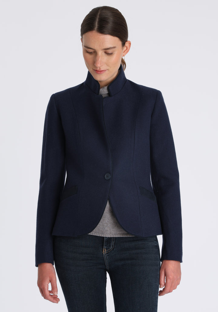 Model wearing the Tallulah jacket in navy textured merino wool with suede trim, a tailored style with a single button fastening and a collar that can be worn turned up or down.