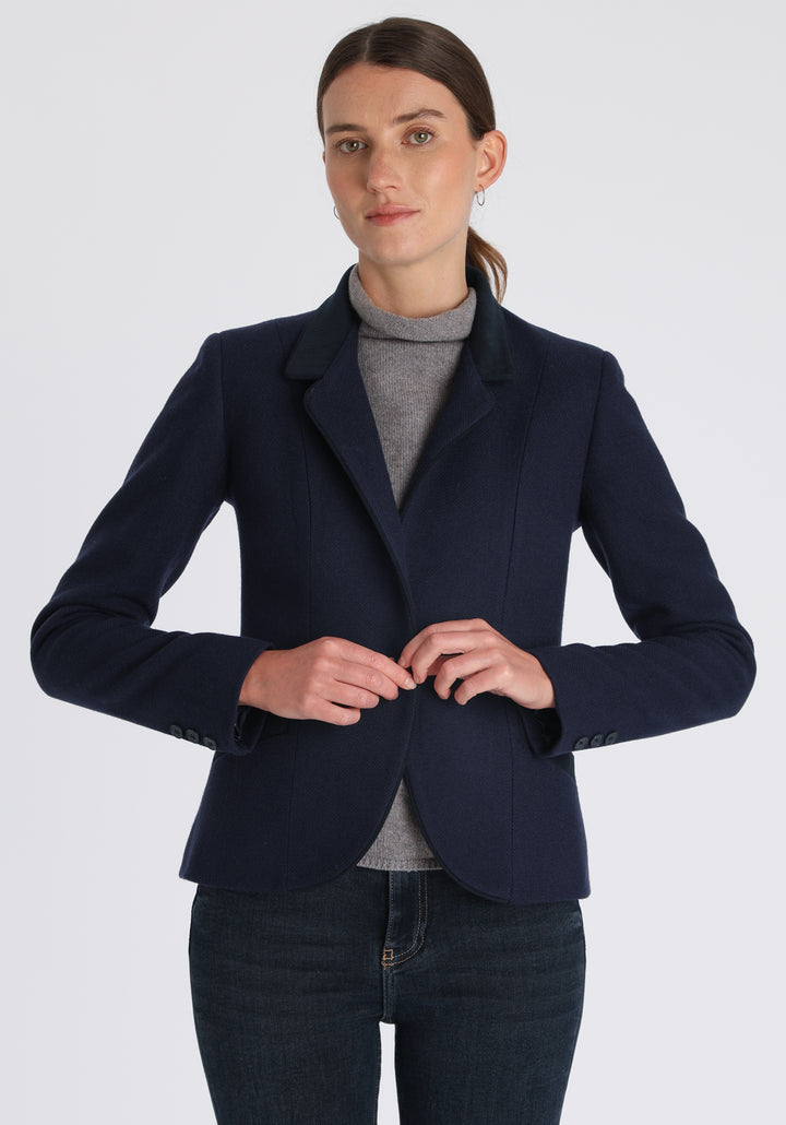 Model wearing the Tallulah jacket in navy textured merino wool with suede trim, a tailored style with a single button fastening and a collar that can be worn turned up or down.