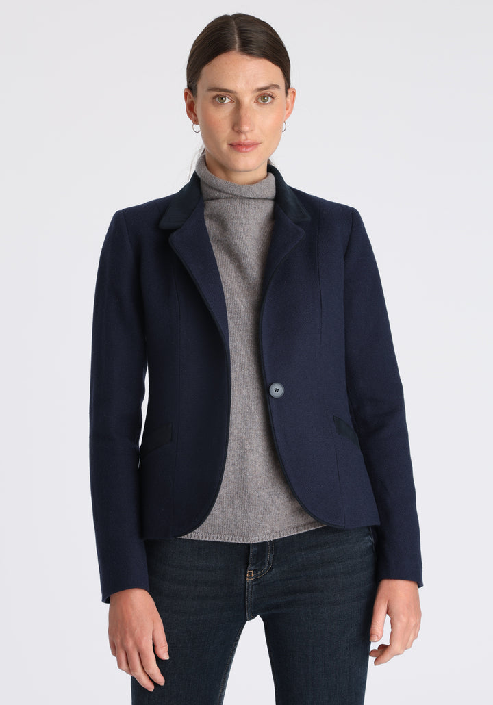 Model wearing the Tallulah jacket in navy textured merino wool with suede trim, a tailored style with a single button fastening and a collar that can be worn turned up or down.
