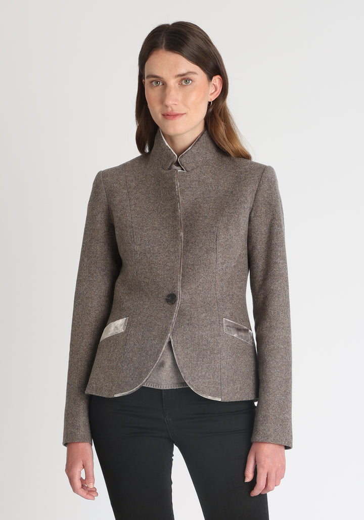 Model wearing the Tallulah jacket in a luxuriously soft cool mallow taupe herringbone lambswool with silk velvet trim, a tailored style with a single button fastening and a collar that can be worn turned up or down.