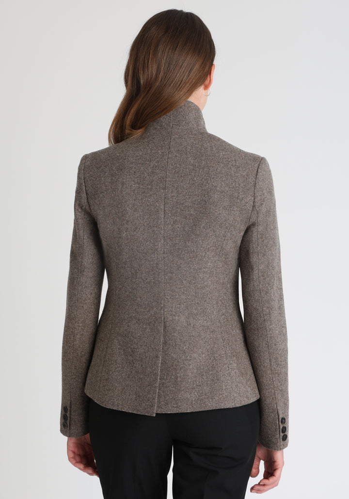 Model wearing the Tallulah jacket in a luxuriously soft cool mallow taupe herringbone lambswool with silk velvet trim, a tailored style with a single button fastening and a collar that can be worn turned up or down.