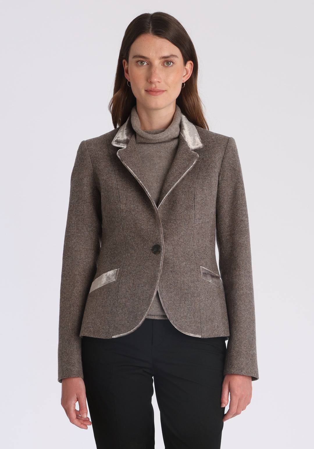 Model wearing the Tallulah jacket in a luxuriously soft cool mallow taupe herringbone lambswool with silk velvet trim, a tailored style with a single button fastening and a collar that can be worn turned up or down.