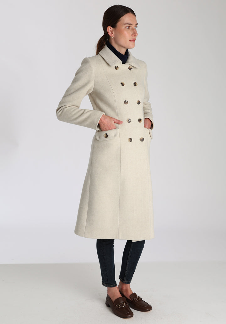 Model wearing the Tori coat in cream merino wool, a vintage-inspired style with a double-breasted front, gently flared skirt, and curved detailing on the collar, pockets, and back belt.