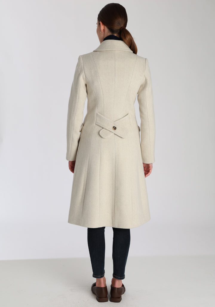 Model wearing the Tori coat in cream merino wool, a vintage-inspired style with a double-breasted front, gently flared skirt, and curved detailing on the collar, pockets, and back belt.