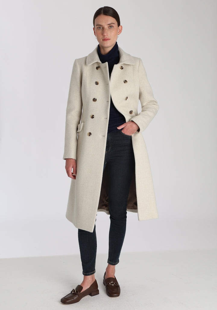 Model wearing the Tori coat in cream merino wool, a vintage-inspired style with a double-breasted front, gently flared skirt, and curved detailing on the collar, pockets, and back belt.