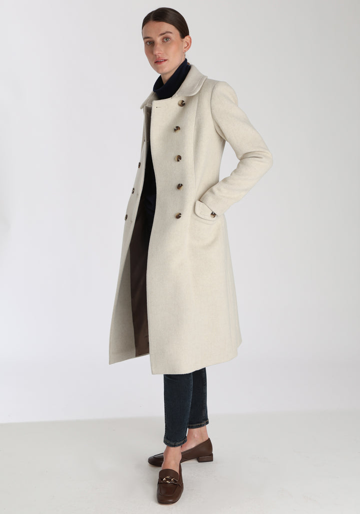 Model wearing the Tori coat in cream merino wool, a vintage-inspired style with a double-breasted front, gently flared skirt, and curved detailing on the collar, pockets, and back belt.