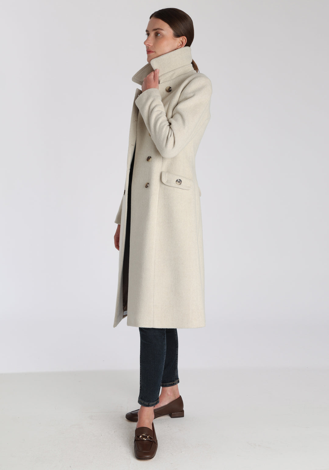 Model wearing the Tori coat in cream merino wool, a vintage-inspired style with a double-breasted front, gently flared skirt, and curved detailing on the collar, pockets, and back belt.