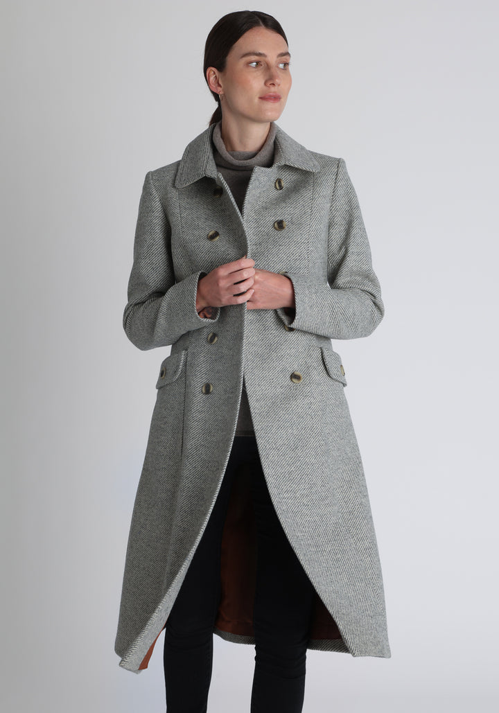 Model wearing the slate blue and cream lambswool twill, a vintage-inspired style with a double-breasted front, gently flared skirt, and curved detailing on the collar, pockets, and back belt.