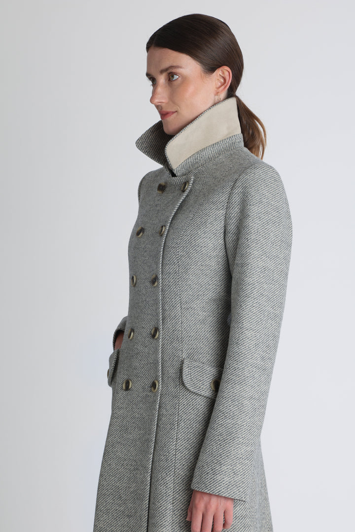 Model wearing the slate blue and cream lambswool twill, a vintage-inspired style with a double-breasted front, gently flared skirt, and curved detailing on the collar, pockets, and back belt.